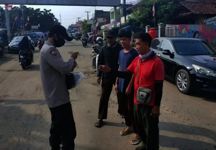 BAGIKAN MASKER–Personel Polsek Labuan, sedang membagikan masker kepada pengguna Jalan, di Jalan Raya Labuan-Carita, tepatnya di wilayah Pasar Labuan, Minggu (24/10/2021). (ISTIMEWA)
