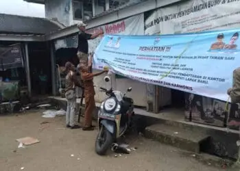 Anggota Satpol PP Kecamatan Menes, memasang spanduk sosialisasi relokasi PKL, Senin (16/1/2023). (ISTIMEWA)