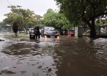 DORONG MOTOR: Salah satu ruas jalan di wilayah Kutabumi, Kecamatan Pasar Kemis, terendam banjir. Sejumlah pengendara sepeda motor terpaksa mendorong kendaraannya karena mogok akibat genangan air, Senin (12/1/2026). (ALFIAN/SATELIT NEWS)