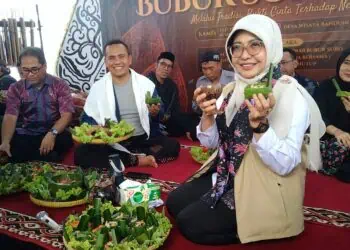FESTIVAL BUBUR SURO - Bupati Pandeglang Raden Dewi Setiani, menunjukkan bubur yang sudah dimasak, saat menghadiri Festival Bubur Suro Desa Bandung, Kecamatan Banjar, Kabupaten Pandeglang, Kamis (25/6/2026). (MARDIANA/SATELITNEWS.COM)