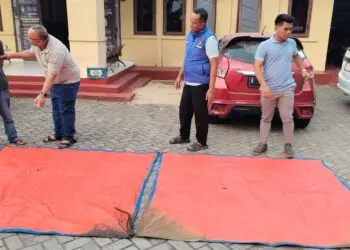 TERPAL : Anggota Polda Banten, menunjukkan terpal hasil temuan pencarian rombongan jurnalis yang hilang di Perairan Selat Sunda. (ISTIMEWA)