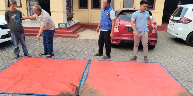 TERPAL : Anggota Polda Banten, menunjukkan terpal hasil temuan pencarian rombongan jurnalis yang hilang di Perairan Selat Sunda. (ISTIMEWA)