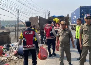 BERSIHKAN SAMPAH -- Petugas Polisi dari Polsek Cikande Polres Serang, bersama personel Dinas Kebersihan dan Pemerintah Kecamatan (Pemkec) Cikande, membersihkan tumpukan sampah liar di tepi Jalan Raya Serang-Jakarta, Desa Parigi, Kecamatan Cikande, Selasa (15/9/2026). (ISTIMEWA)
